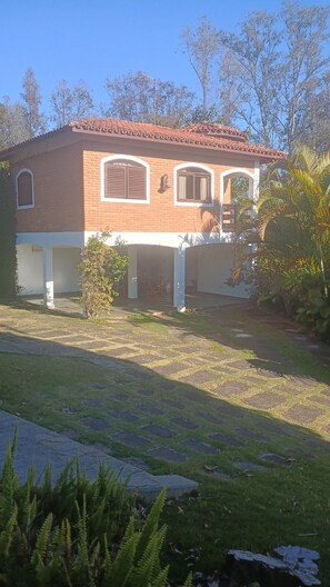 Una casa de dos pisos con techo de tejas, un patio cubierto y un jardín.