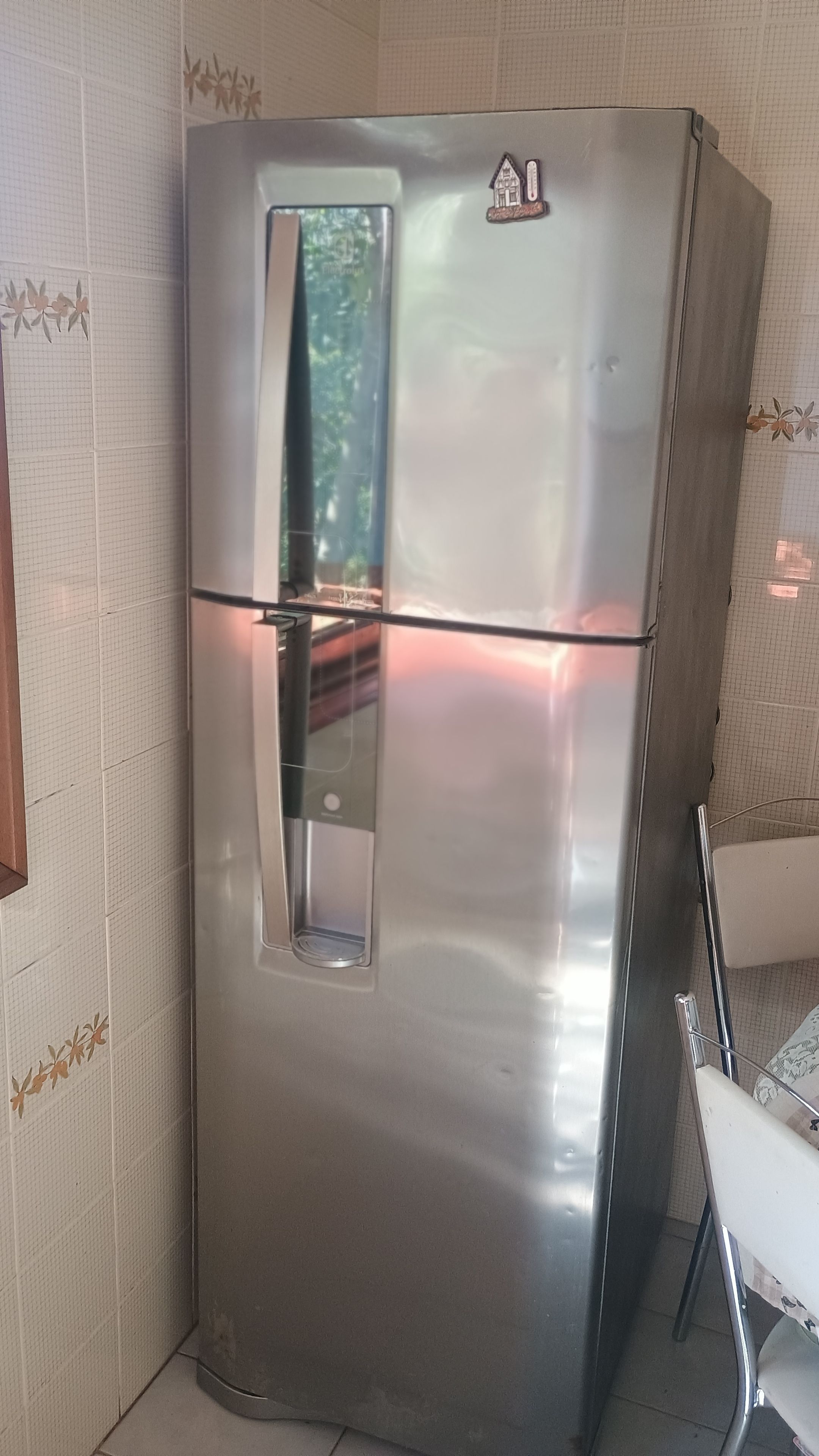 A stainless steel refrigerator with a freezer compartment, located in a corner of a room with patterned wallpaper.