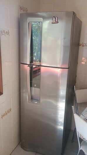 Un refrigerador de acero inoxidable con compartimento congelador, ubicado en un rincón de una habitación con papel tapiz estampado.