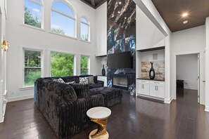 A spacious living room with a large black sofa, a white coffee table, and a fireplace.
