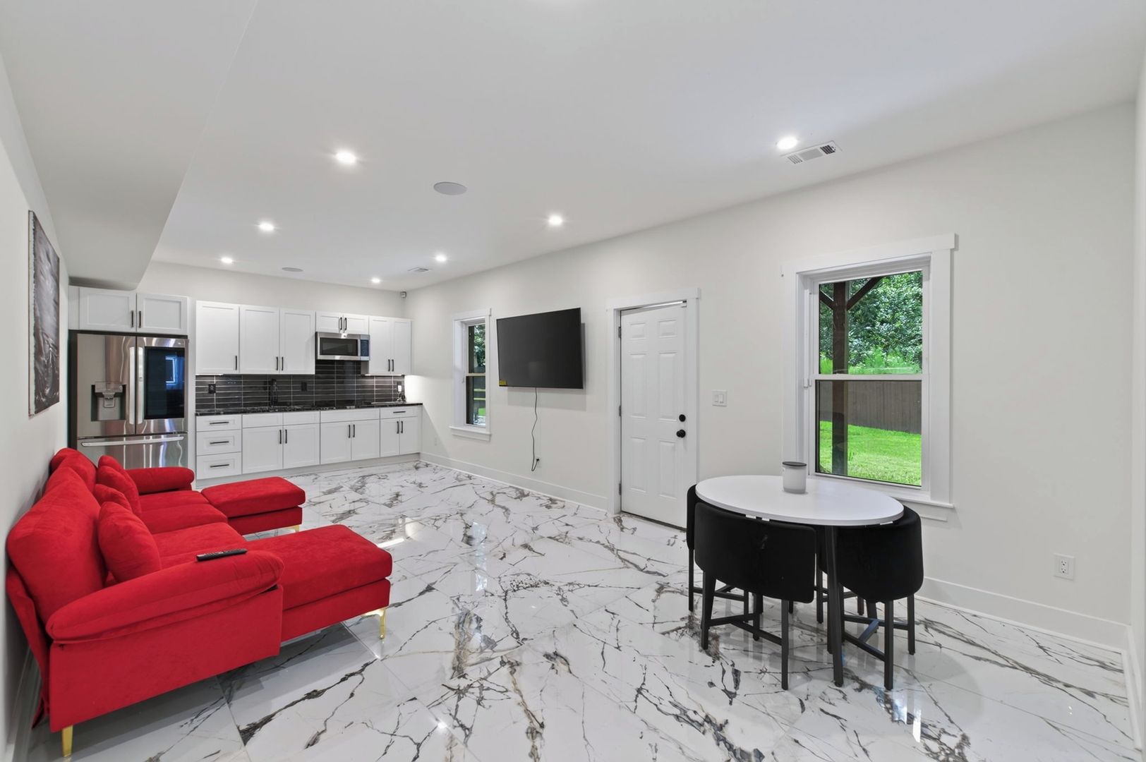 A modern kitchen with white cabinets, a built-in oven, and a flat-screen TV.