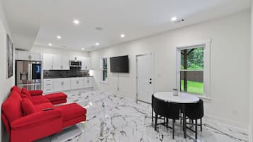 A modern kitchen with white cabinets, a built-in oven, and a flat-screen TV.