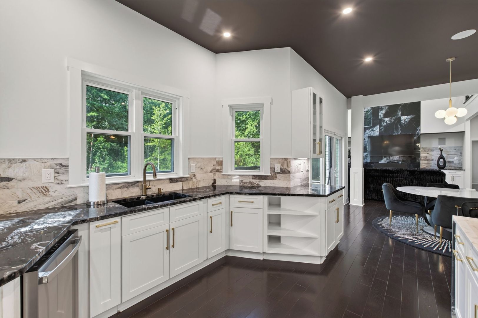 A modern kitchen with white cabinetry, a black countertop, and a dining area with a round table and chairs.