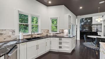 A modern kitchen with white cabinetry, a black countertop, and a dining area with a round table and chairs.