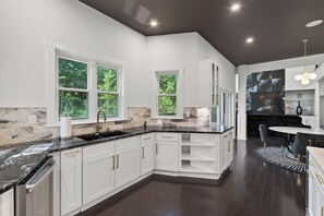 A modern kitchen with white cabinetry, a black countertop, and a dining area with a round table and chairs.