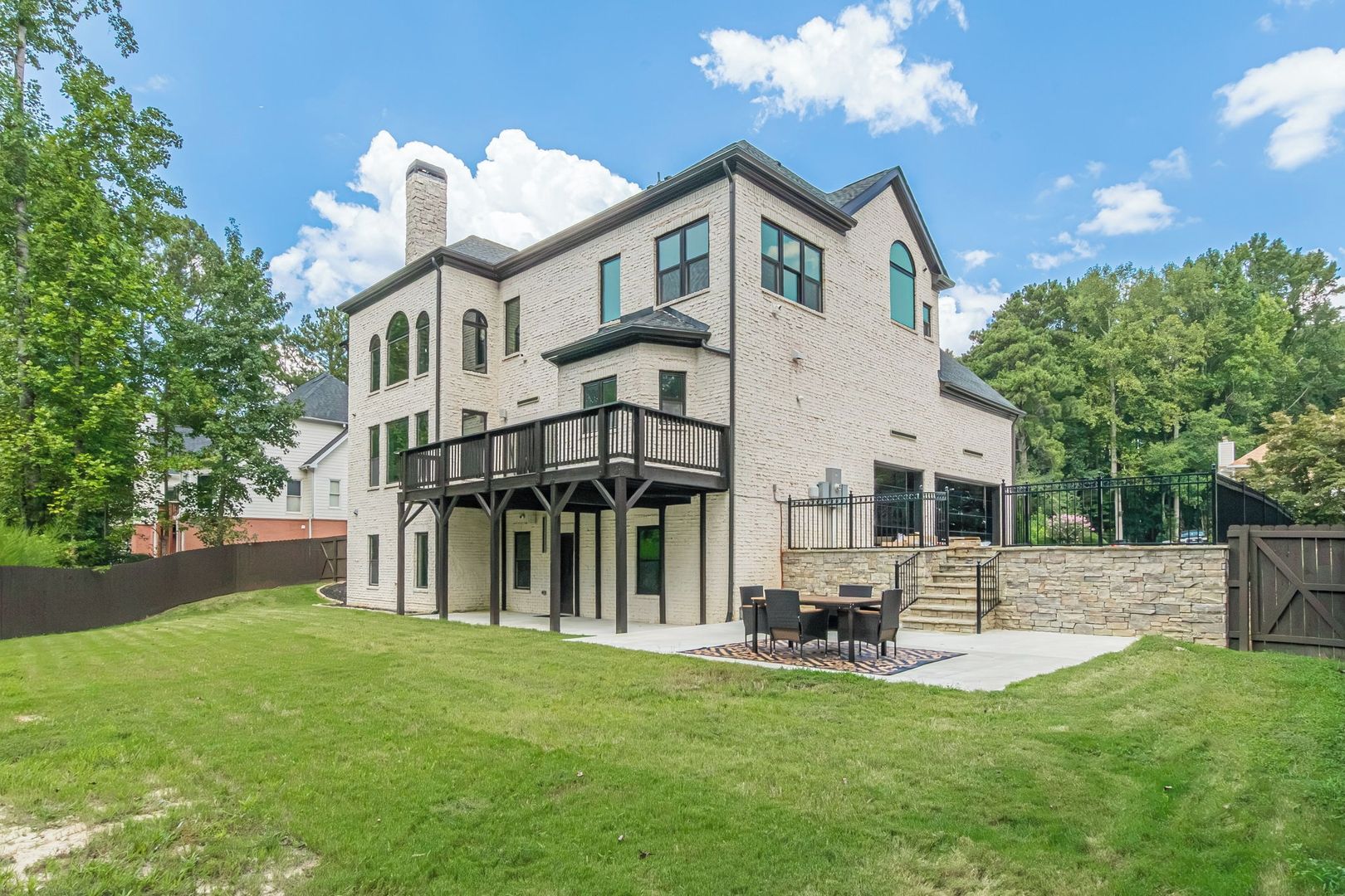 A two-story house with a balcony, a stone wall, and a grassy yard.