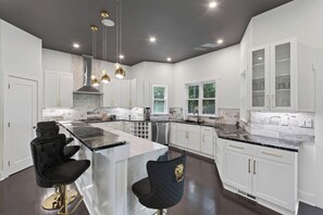 A modern kitchen with a large island, white cabinetry, and pendant lighting. - Home Theater • Patio • Sleeps 12 (Stonecrest)