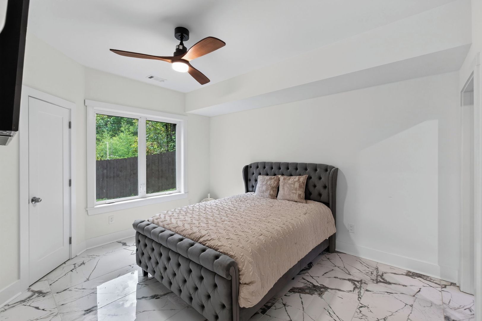 A bedroom with a bed, a ceiling fan, a window, and a door.