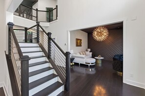A modern interior with a staircase, a living area with a sofa and a round coffee table, and a unique wall-mounted light fixture. - Home Theater • Patio • Sleeps 12 (Stonecrest)