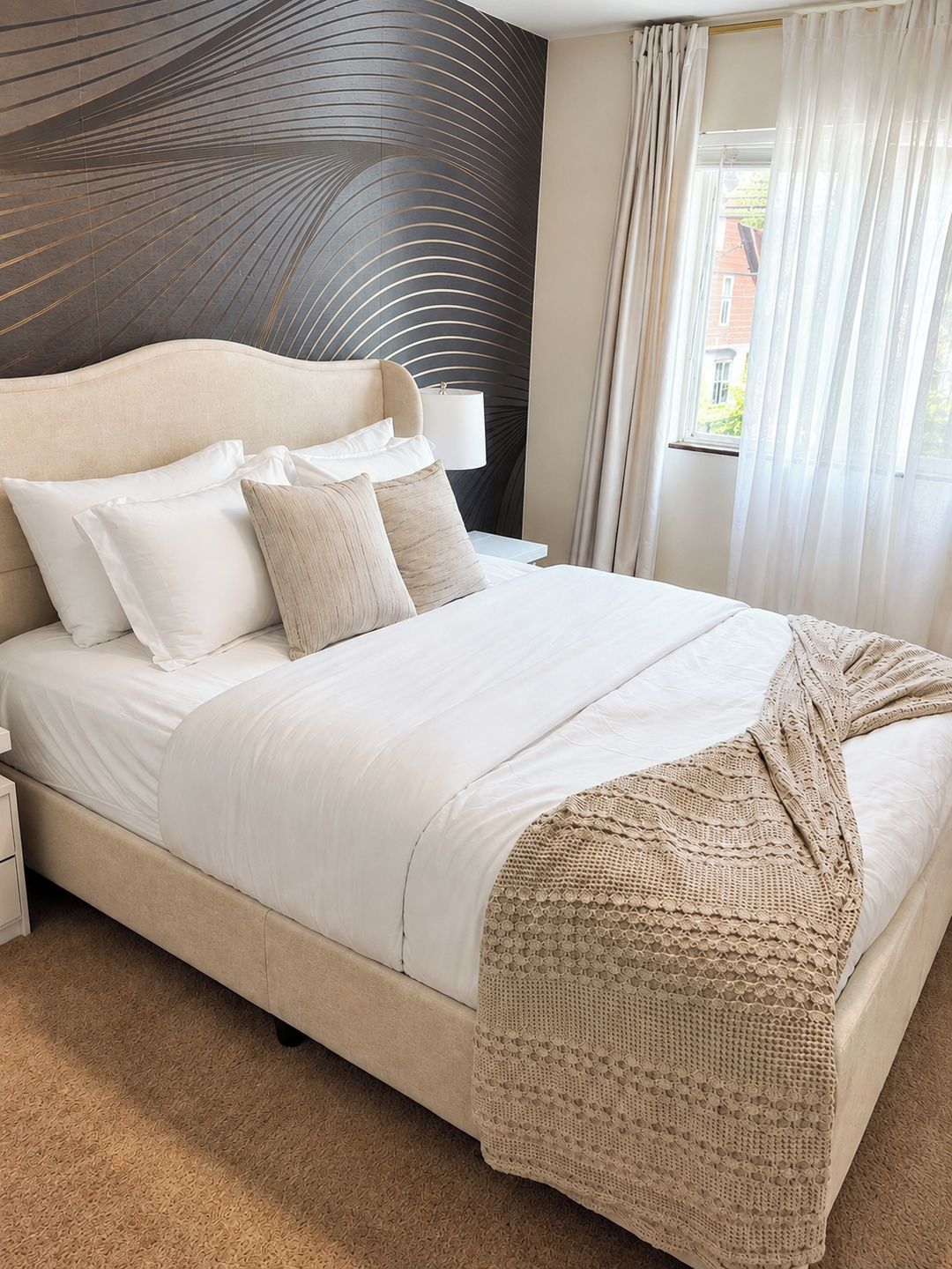 Un dormitorio con una cama grande, cabecera de diseño único, lámpara de noche y vistas al exterior a través de una ventana.