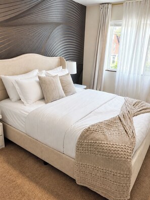 A bedroom with a large bed, a headboard with a unique design, a bedside lamp, and a view of the outside through a window.