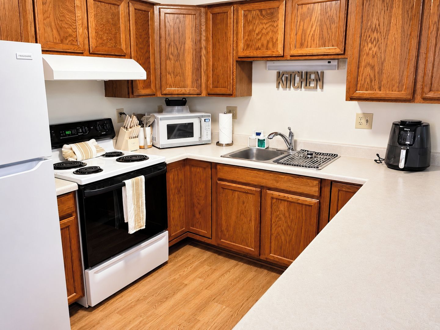 Una cocina con armarios de madera, un refrigerador blanco, estufa, microondas, pileta y cafetera.