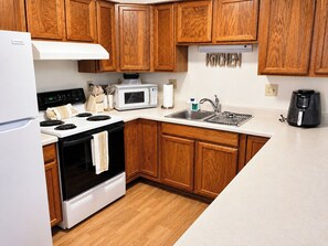 A kitchen with wooden cabinets, a white refrigerator, a stove, a microwave, a sink, and a coffee maker.