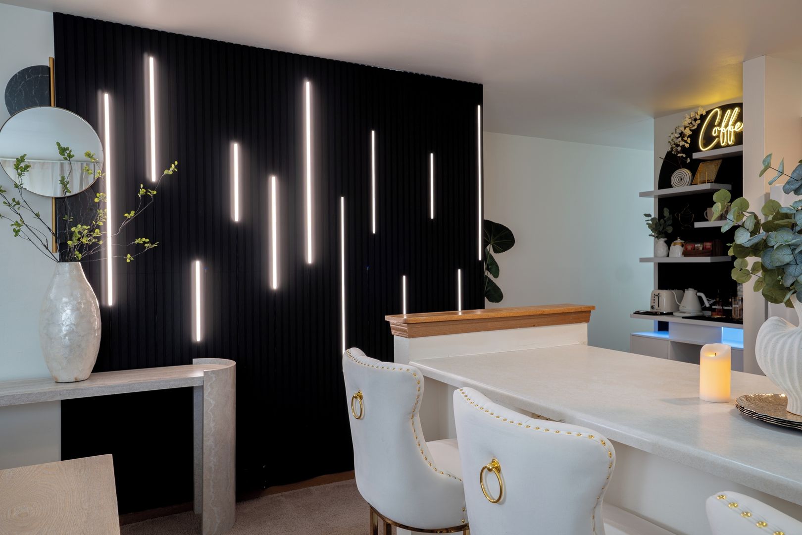 A modern kitchen with a black backdrop, white chairs, a wooden countertop, and a neon sign.