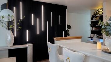 A modern kitchen with a black backdrop, white chairs, a wooden countertop, and a neon sign.