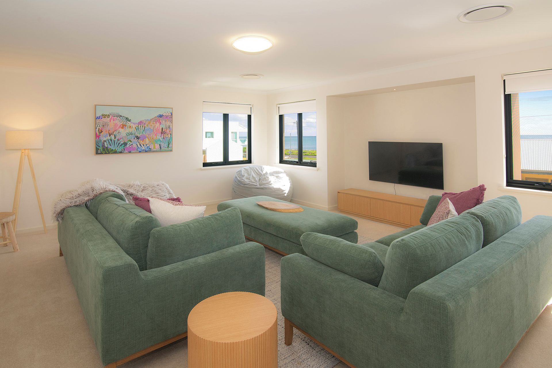 A living room with green sofas, a flat-screen TV, a painting, and a lamp.