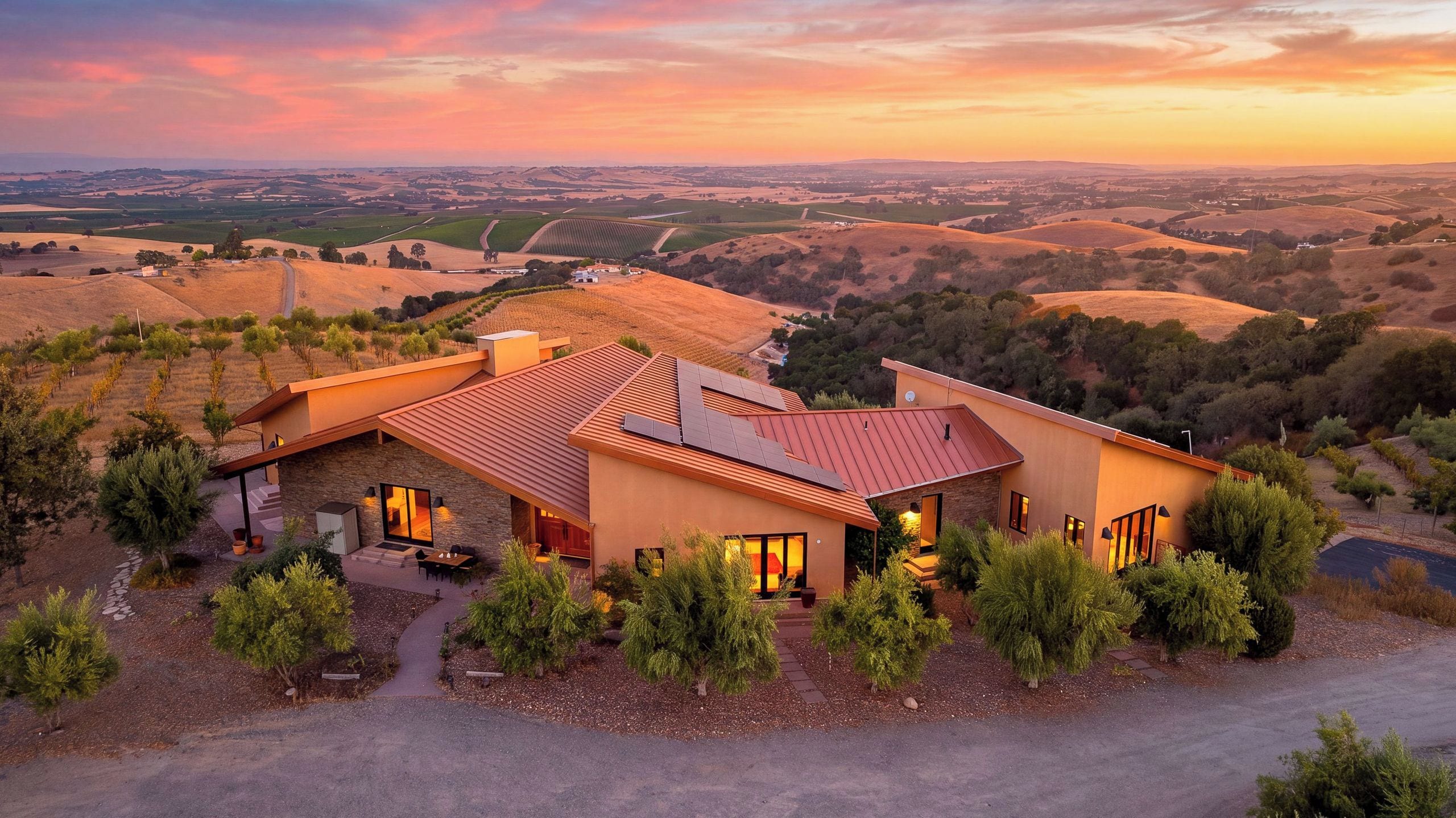 Une maison moderne avec un toit rouge, entourée d’un jardin aménagé et de vignobles.