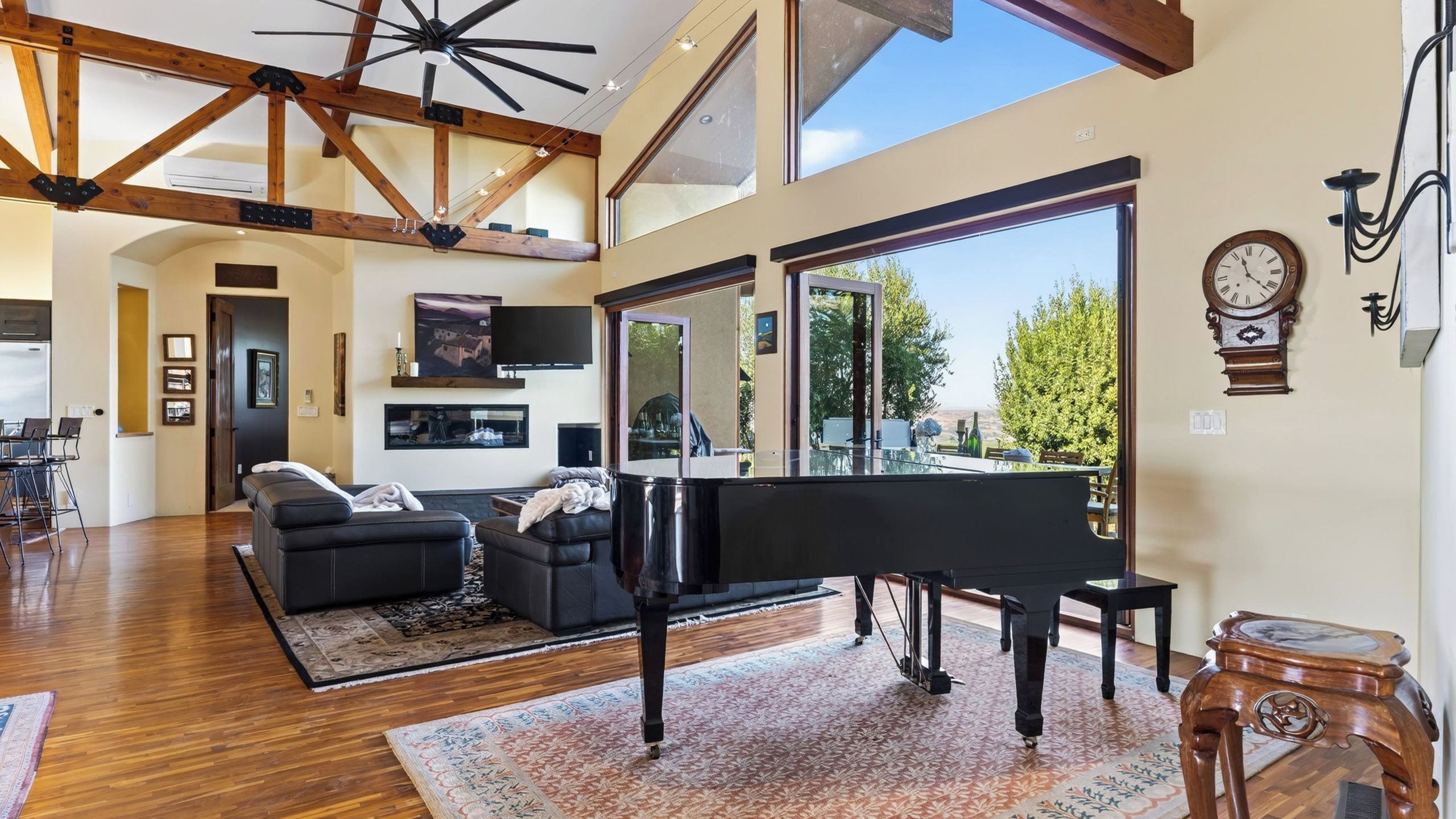 A spacious living room with a grand piano, a comfortable sofa, and a large window offering a view of the outdoors.
