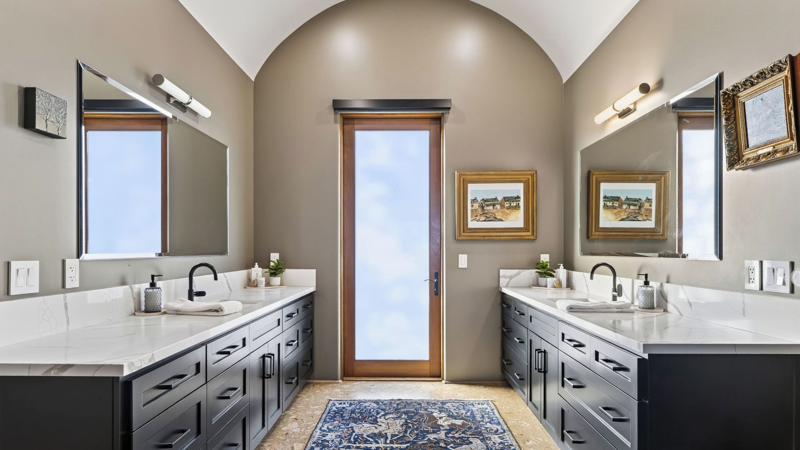A modern bathroom with two sinks, a large mirror, and a door leading to a balcony.