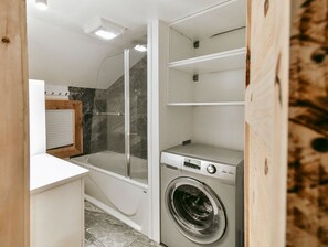 Ein kleiner Waschraum mit Waschmaschine, einer behindertzugänglichen Dusche und einer weißen Arbeitsplatte.