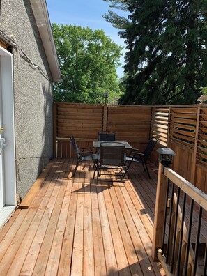 Eine Holzterrasse mit Tisch, Stühlen, einem Grill und einem Holzzaun.