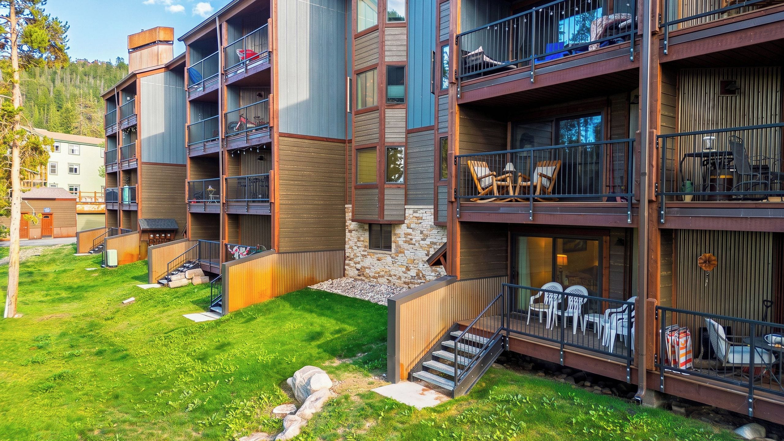A multi-story building with balconies, outdoor seating, and a stone wall.