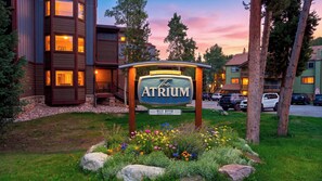 A hotel sign with 'The Atrium' prominently displayed, surrounded by a landscaped garden with various flowers and a parking area with several cars. - Ski Casa Azul by Avantstay Ski Shuttle + Walk to Main St Shared Hot Tub + Grill (Breckenridge)