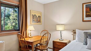 Ein Hotelzimmer mit einem Holztisch, zwei Stühlen, einem Bett mit Kissen, einem Nachttisch, einer Lampe und einem gerahmten Bild an der Wand.