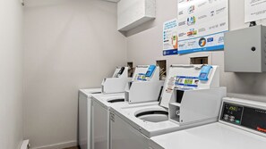 Eine Wäscherei mit mehreren Waschmaschinen und Trocknern, Bedienfeldern und Informationsplakaten an den Wänden.