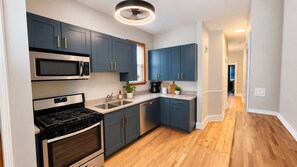 A modern kitchen with dark blue cabinets, stainless steel appliances, and a wooden floor. - Duplex - Both Units - 2 Kitchens - Privacy - Fenced Yard (Oak Park)