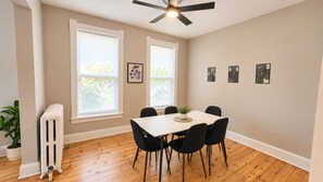 A dining area with a white table and black chairs, a ceiling fan, and a radiator. - Duplex - Both Units - 2 Kitchens - Privacy - Fenced Yard (Oak Park)