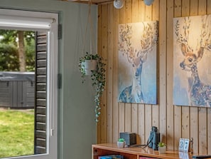 Ein Zimmer mit Holzwandverkleidung, einem Fenster mit Jalousien, einer hängenden Pflanze, zwei Hirschbildern, einem Teleskop und einem kleinen Tisch mit Pflanze und einer Nummer.