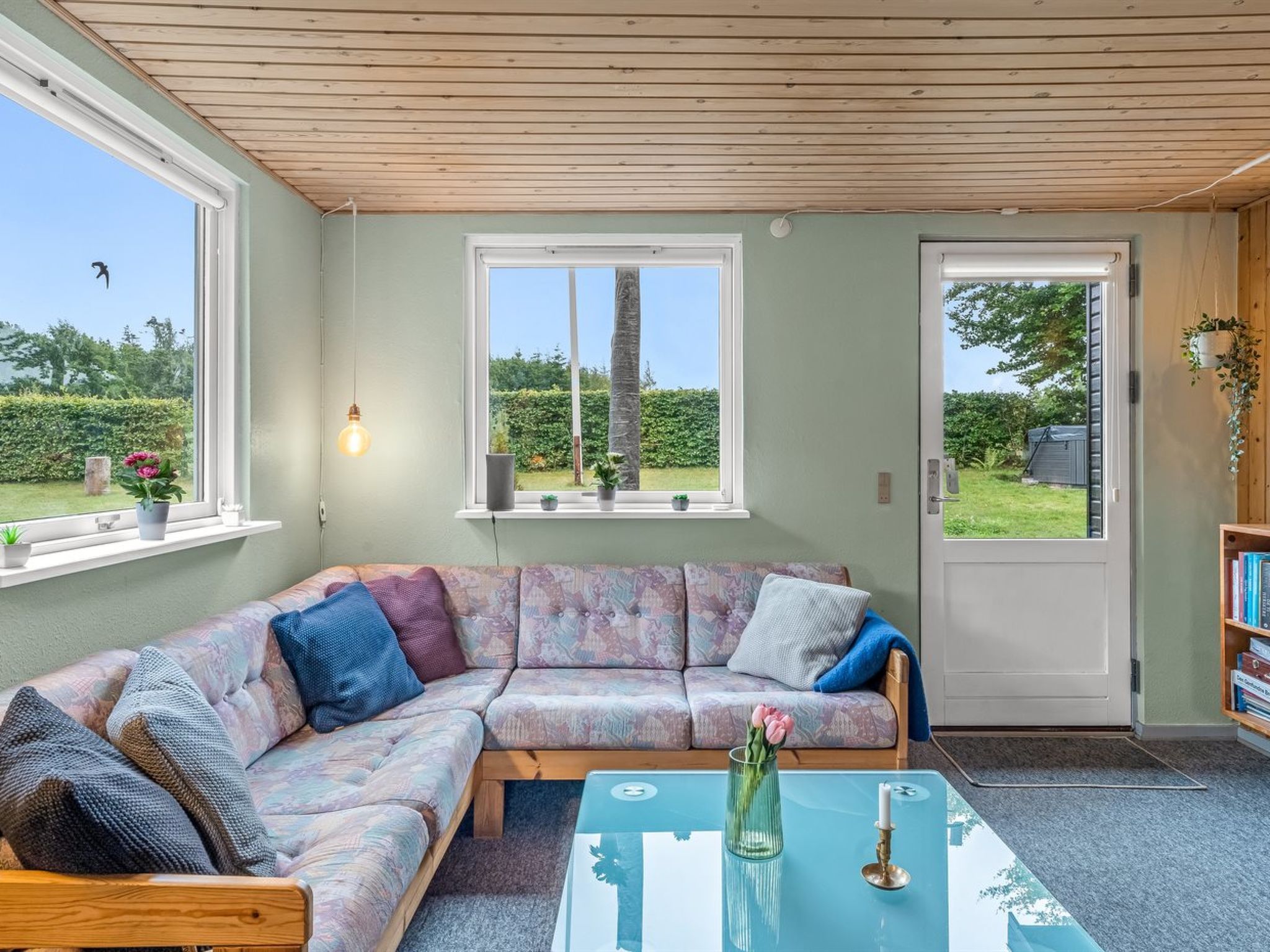 A cozy living room with a sectional sofa, a glass coffee table, and a door leading to a garden.