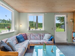 Ein gemütliches Wohnzimmer mit einer Eckcouch, einem Glastisch und einer Tür, die in einen Garten führt.