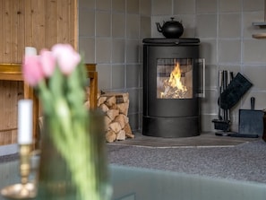 Ein moderner Kamin mit sichtbarem Feuer, ein Holzstoß und eine Vase mit Blumen.