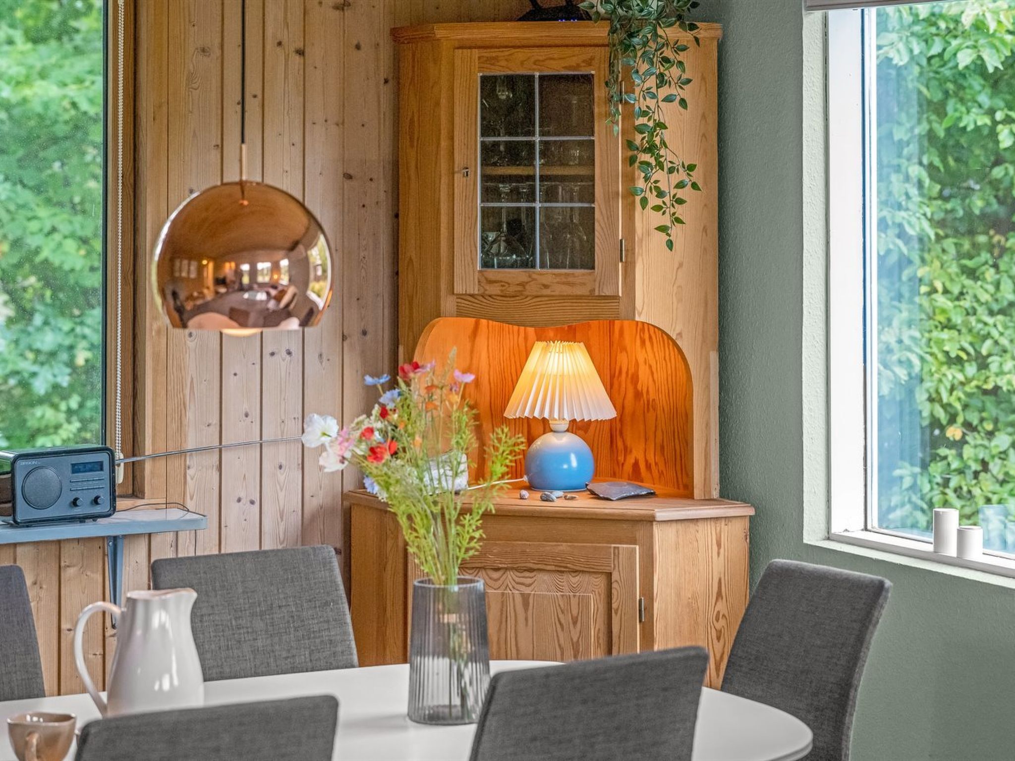 Un intérieur en bois avec un miroir rond, une table avec des chaises, une lampe et une radio.