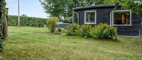 A modern log cabin with a grassy yard, a picnic table, and a hedge.