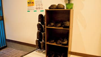 A wooden shoe rack with multiple shelves against a wall, next to a no parking sign and a potted plant.