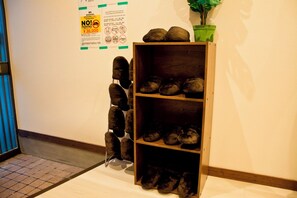 A wooden shoe rack with multiple shelves against a wall, next to a no parking sign and a potted plant. - Nagayama tei (Asahikawa)