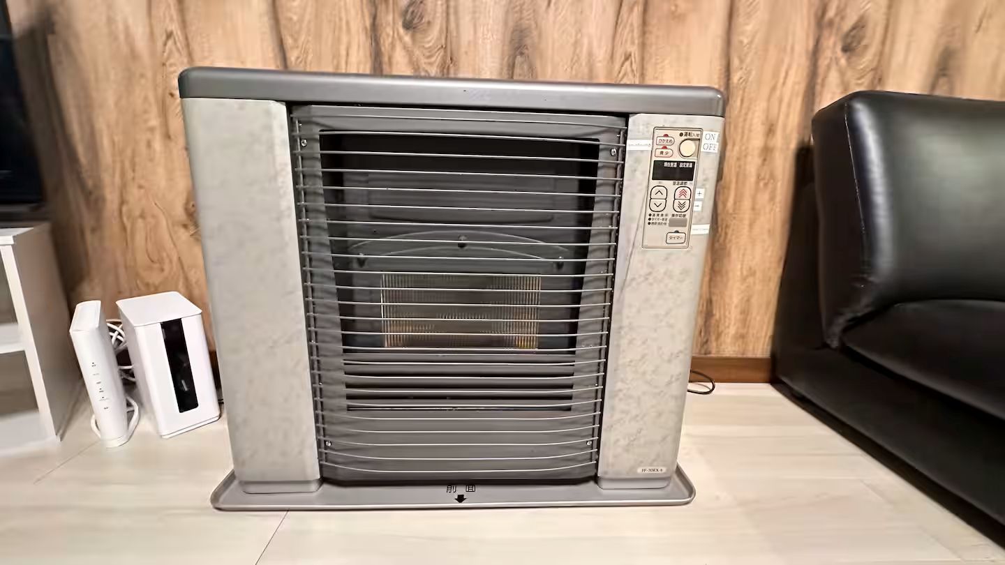 A room with a standing heater, a black leather sofa, and two white electronic devices.