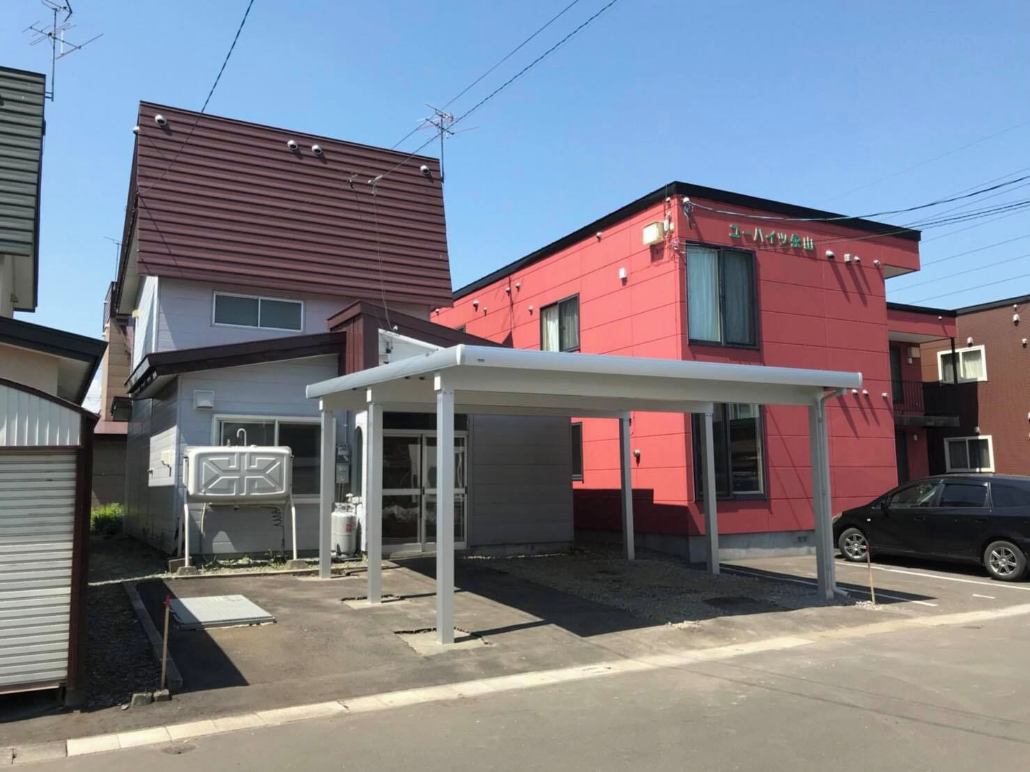 A red building with a covered entrance and a black car parked nearby.