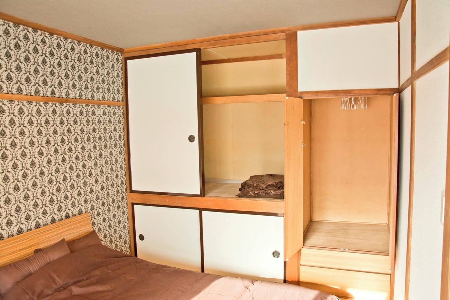 Una habitación con una cama, un armario con varios compartimentos y un papel tapiz estampado.