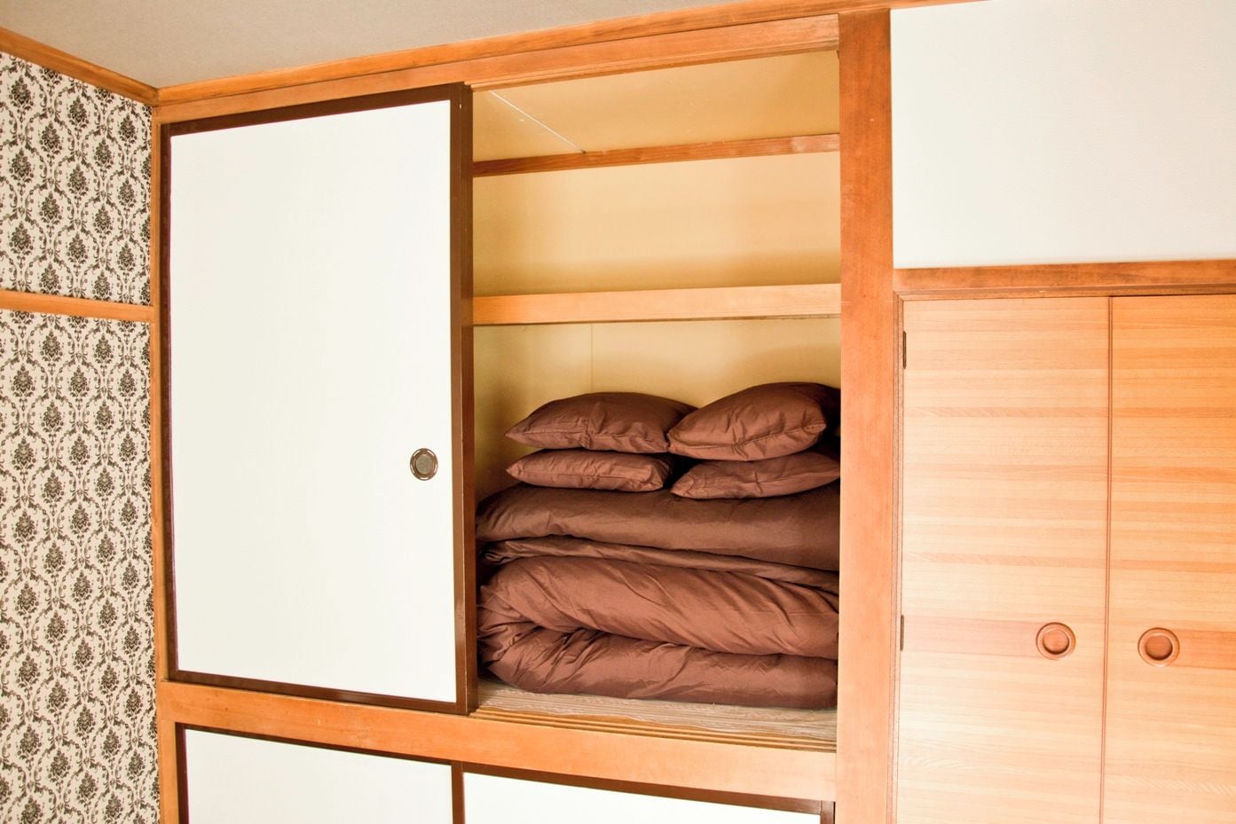 A wardrobe with a sliding door, a bed with brown bedding, and patterned wallpaper.