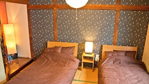 Ein Zimmer mit zwei Betten, jedes mit einem Holz-Kopfteil, einem Nachttisch mit Lampe und einer Wand mit floralem Muster.