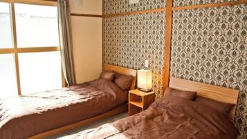 A room with two beds, a nightstand with a lamp, and patterned wallpaper.