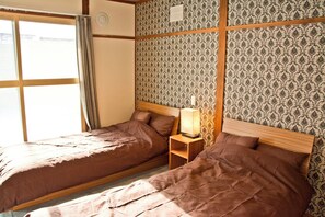 A room with two beds, a nightstand with a lamp, and patterned wallpaper. - Nagayama tei (Asahikawa)
