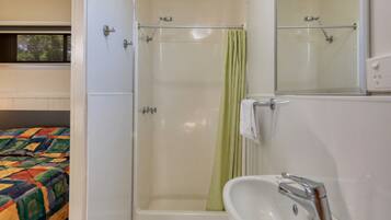 Ein Badezimmer mit Dusche, Waschbecken und einem Bett mit einer farbenfrohen Steude.