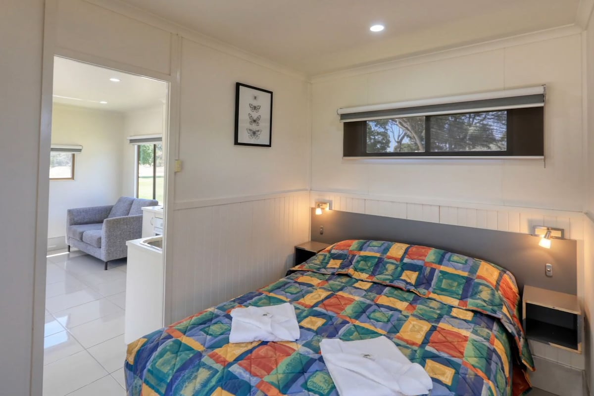 A bedroom with a bed, bedside tables, a window, and a view of another room.
