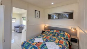 A bedroom with a bed, bedside tables, a window, and a view of another room. - Swan Hill Lifestyle Park (Swan Hill)
