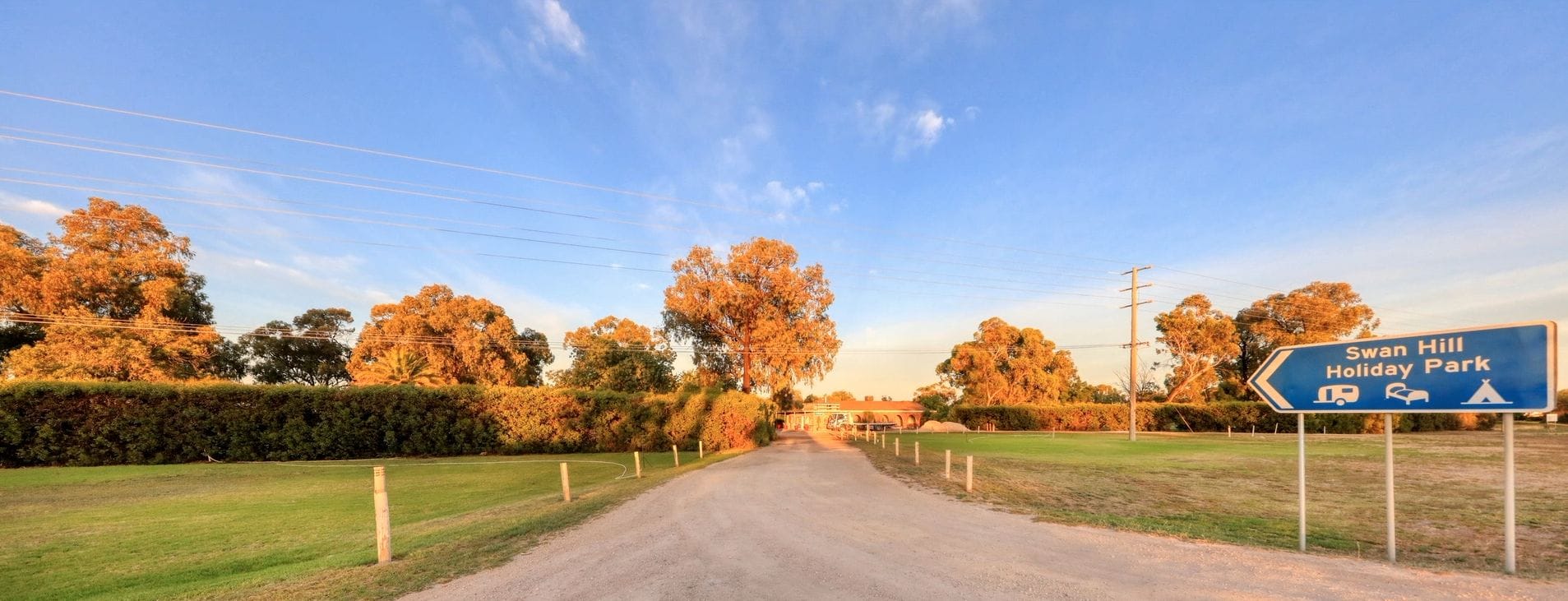 Eine ländliche Straße, die zum Swan Hill Holiday Park führt, mit einem Wegweiser.
